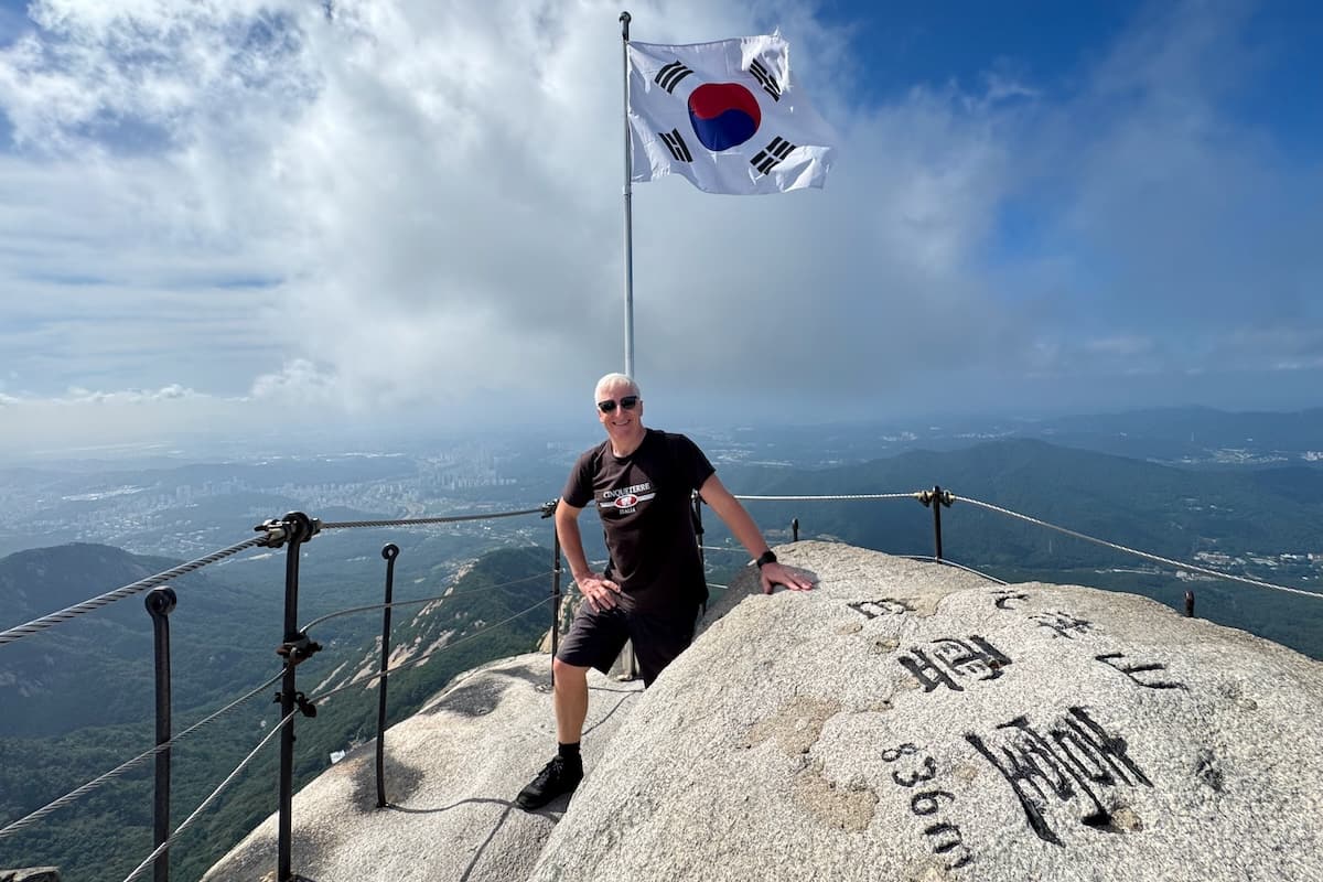 Man smiling at Bukhanson Peak with Korean flag and inscription on rock