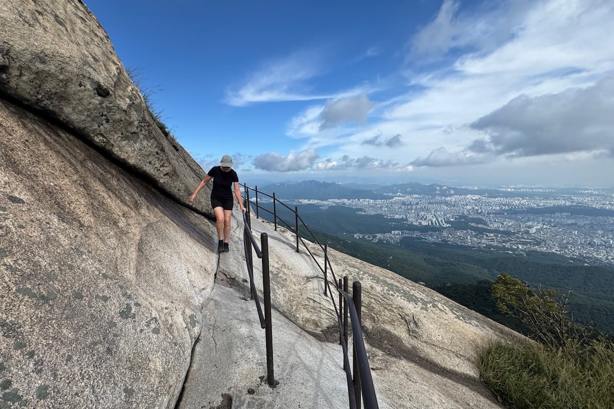 Woman holding rail at Bukhansan Peak with views of Seoul in the distance